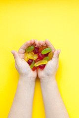 Child with a handful of candies on a yellow background