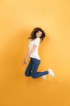 Emotional woman jumping isolated over yellow background