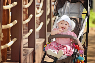 funny baby girl sitting in the stroller at the summer park