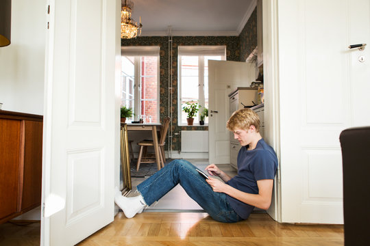 Side view of young man using digital tablet while sitting at doorway