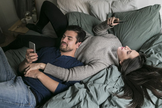 High angle view of couple using mobile phone while relaxing on bed at home