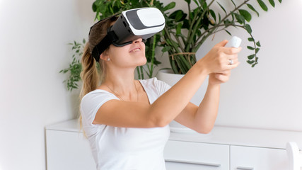 Happy young woman in VR headset holding game controller and playing video games