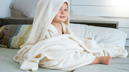 Portrait of cute 1 year old toddler boy sitting under big towel after having bath