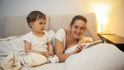 Adorable toddler boy watching as his mother using digital tablet in bed