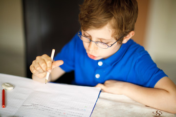 Naklejka na ściany i meble Cute little kid boy with glasses at home making homework, writing letters with colorful pens.