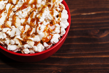 popcorn in a red bowl of poured caramel, on a dark table