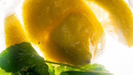 Macro backlit image of lemons and mint leaves in carbonated water