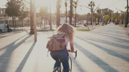 Slow motion of young pretty woman, student or teenager commuting to work or school on commuter road bicycle through city park in beautiful sunset light. enjoy hipster lifestyle with backpack