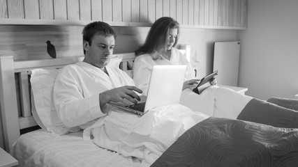 Black and white image of young couple of businessman and businesswoman working in bed at morning