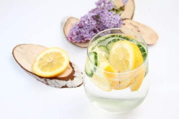 Detox flavored water with lemon and cucumber on white background with lilac and wood decoration. Healthy food concept.  Refreshing summer homemade cocktail. Copy space. No sharpen. 