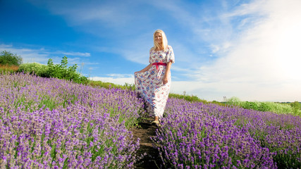 Beautiful smiling woman walking between rows of blooming lavender flowers