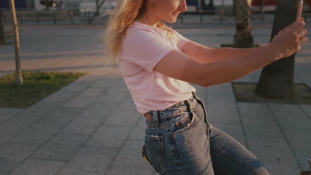 Careless young woman with blonde hair, silly and oblivious to world makes selfies and texts on smartphone while riding bicycle without hands traffic violation, almost crashes
