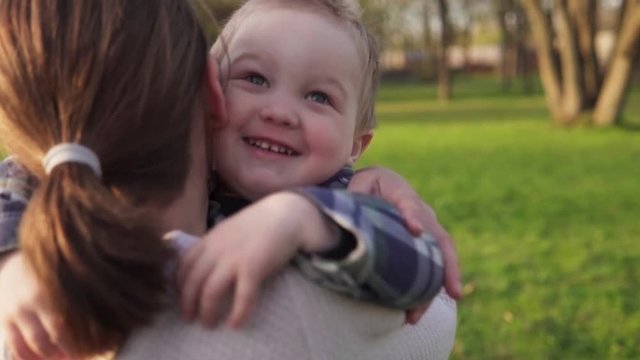 Happy little boy runs into mother's open armsa nd hugs her in spring park