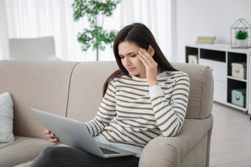 Obraz premium Young woman suffering from headache while sitting on sofa at home