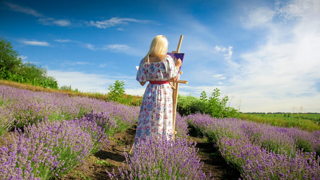 Rear view image of young female artist painting picture of lavender field