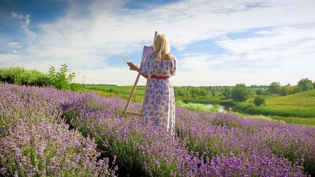 Beautiful young woman in long dress painting picture of lavender field with oil paints