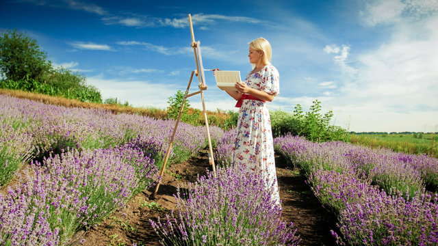 Beautiful young woman with easel drawing lavender field