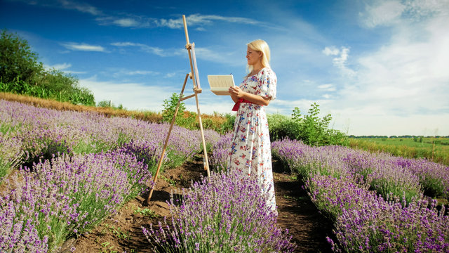 Young blonde woman standing at easel and drawing picture of lavender field