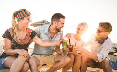 Group of happy millenial friends having fun at beach party drinking cocktail at sunset - Summer joy and friendship concept with young people on vacation - Warm sunshine filtered color tones