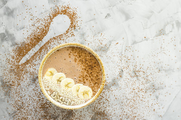 Chocolate-banana smoothies in a bowl on a gray concrete background next to the shape of a spoon of cocoa. Healthy Breakfast Concept