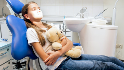 Little girl sitting in dentist chair with toy teddy bear in clinic
