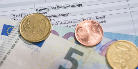 Ausschnitt einer Gehaltsabrechnung mit Münzen und Euroscheinenau