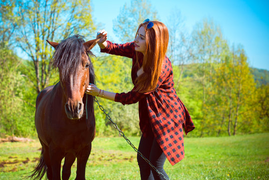 Young woman taking care and talking to a horse on a hot autumn day at village. Beautiful young female walking and hugging with her brown horse outdoor 