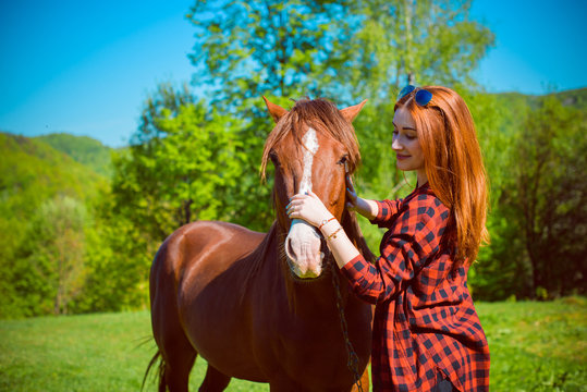 Young woman taking care and talking to a horse on a hot autumn day at village. Beautiful young female walking and hugging with her brown horse outdoor 