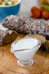 Cream sauce in a transparent glass bowl on wooden board.