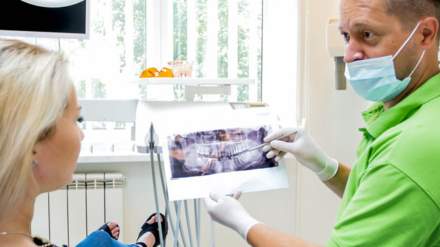 Portrait of dentist talking to his patient and showing x-ray image