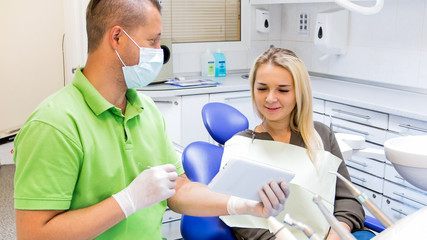 Obraz premium Portrait of male dentist explaining teeth treatment to young woman using digital tablet