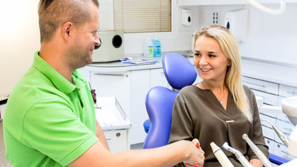 Portrait of satisfied smiling woman shaking hands with dentist after teeth treatment