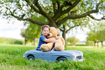 Little preschool kid girl driving big toy car and having fun with playing with big plush toy bear