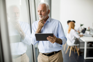 Senior businessman standing by window with digital tablet in his hand