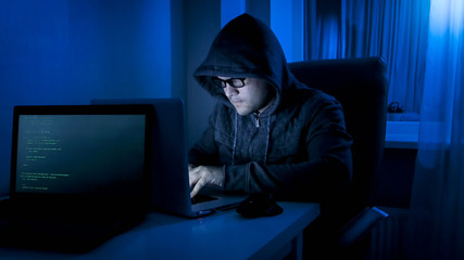 Portrait of hacker criminal working on laptop at night