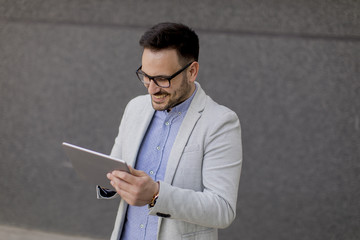 Young businessman with digital tablet by the grey wall