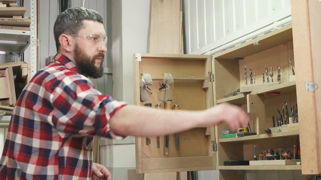 man carpenter in a shirt with a beard uses tools in the workshop close up