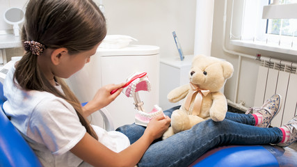 Portrait of little girl educating her teddy bear about teeth hygiene in dentist office