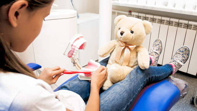 Closeup image of cute girl playing with teddy bear and pretending to be dentist