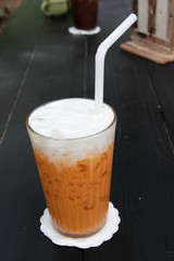 Iced Thai milk tea with  milk foam in a glass on wooden table.