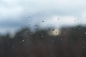 The drops of rain flow down on the dusty glass. Background is blurred.
