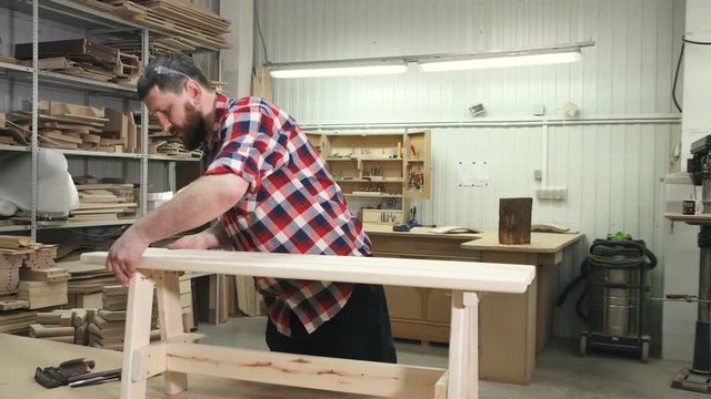 carpenter working in a shirt with a beard in the workshop makes a wooden bench