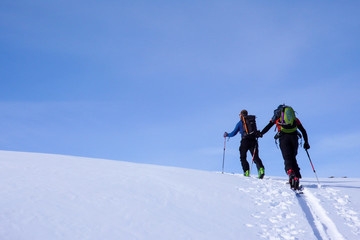 mountain guide on backcountry ski tour leading a client to the peak of a high alpine mountain