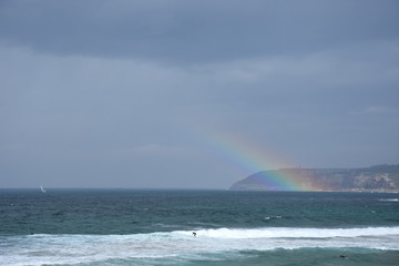 Rainbow over the Tasman sea. Seascape with beautiful multicoloured rainbow over the sea and Curl Curl beach, Australia. Surfers in the water.