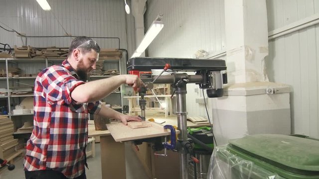 man carpenter in a shirt using drilling machine in workshop