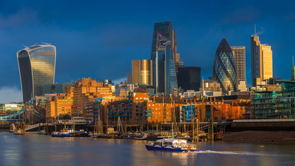 London, England - Skyscrapers of Bank, the leading financial district of London at golden hour with sightseeing boat and colorful dark sky and clouds