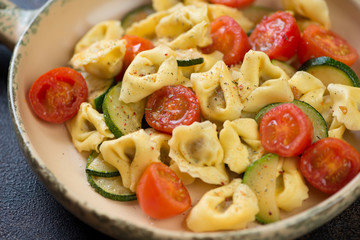 Close-up of italian tortellini with fried zucchini and cherry tomatoes, selective focus, studio shot