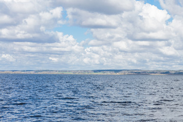 fishing lake: body of water with low waves under summer cloudy sky, forest and hills on the horizon