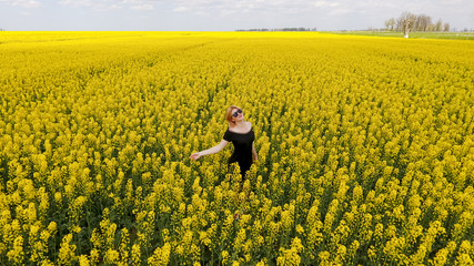 A girl in a black dress among the colors of rape in the field. Walk the girl among the yellow flowers. Flowering rape.