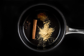 Ingredients for mulled wine in the pan: clove, cinnamon stick, ground ginger, ground pepper. Close up, top view